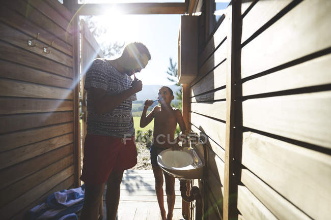Father and son brushing teeth in sunny campsite bathroom — Stock Photo