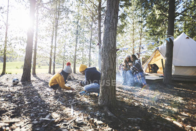 Lesbian couple watching kids gathering kindling at sunny campsite in woods — Stock Photo