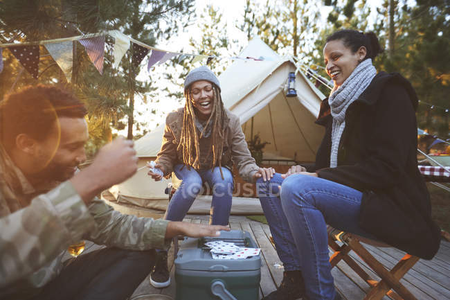 Amigos felices jugando a las cartas en el camping - foto de stock
