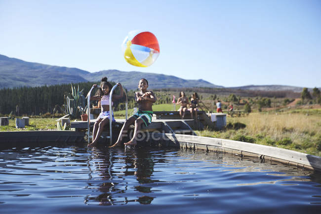 Portrait of playful brother and sister with beach ball at sunny, summer poolside — Stock Photo
