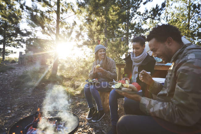 Happy friends eating at sunny campsite in woods — Stock Photo