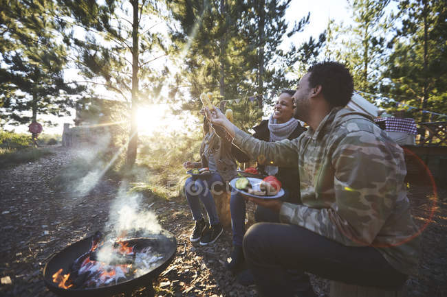 Happy friends eating at sunny campsite in woods — Stock Photo