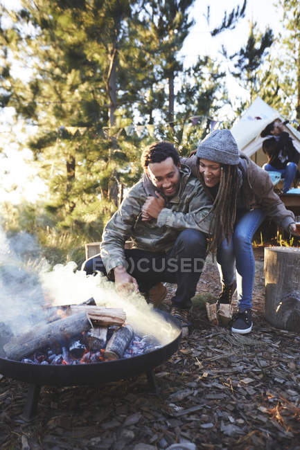 Casal feliz tendendo a fogueira no parque de campismo na floresta — Fotografia de Stock