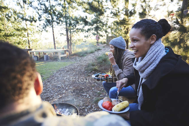 Amigos felices comiendo en el camping en el bosque - foto de stock