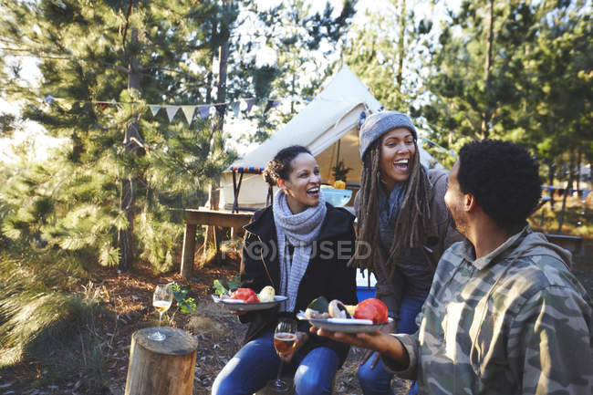 Amici felici ridendo e mangiando al campeggio nel bosco — Foto stock