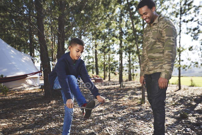 Father watching son breaking kindling at campsite in woods — Stock Photo