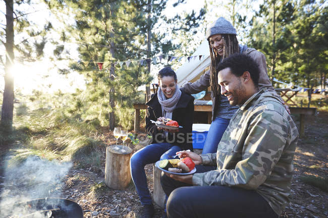 Amigos felizes comendo no acampamento ensolarado — Fotografia de Stock