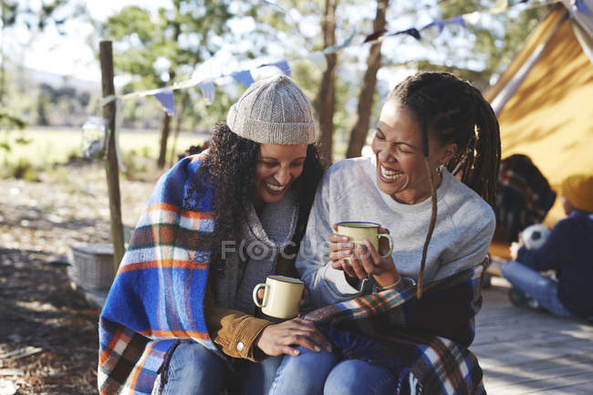 Счастливая, беззаботная лесбийская пара смеется, пьет кофе в кемпинге — стоковое фото
