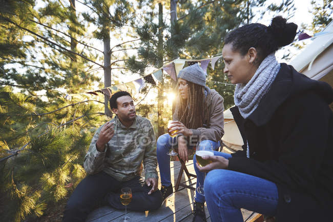 Friends drinking wine and talking at sunny campsite in woods — Stock Photo