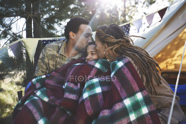 Счастливые любящие родители целуются с сыном, отдыхают в кемпинге — стоковое фото