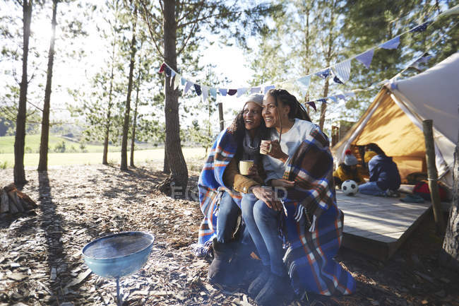 Happy lesbian couple relaxing, drinking coffee at sunny campsite in woods — Stock Photo