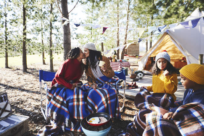 Affectionate lesbian couple with kids kissing at sunny campsite in woods — Stock Photo