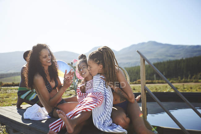 Cariñosa pareja lesbiana e hija en remoto, soleado, verano piscina - foto de stock