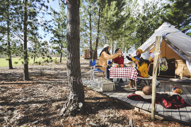 Lesbian couple and kids toasting mugs at sunny campsite table in woods — Stock Photo
