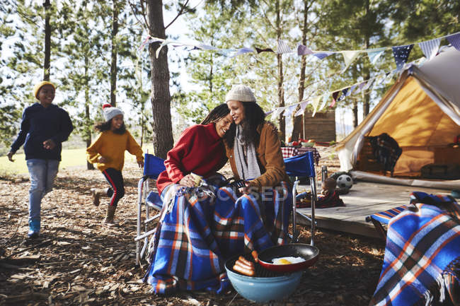 Happy, affectionate lesbian couple with kids relaxing at campsite in woods — Stock Photo