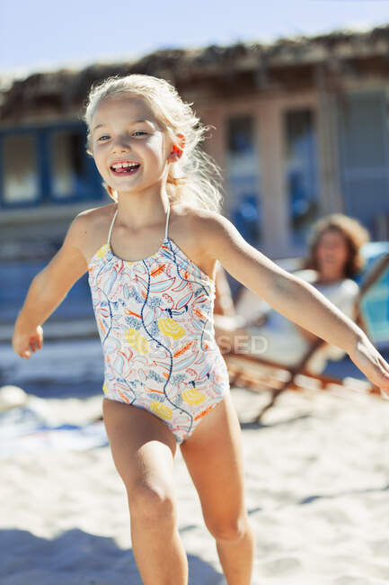 Menina despreocupada em roupa de banho correndo na praia ensolarada — Fotografia de Stock