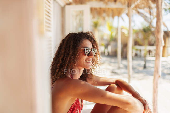 Happy, carefree young woman relaxing on sunny beach hut patio — Stock Photo