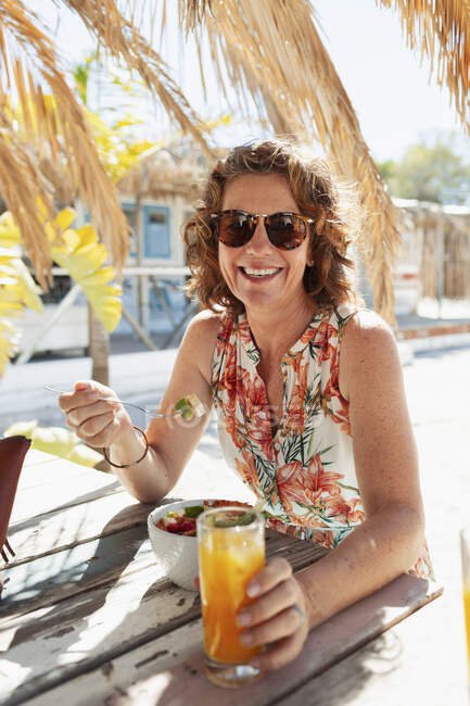 Portrait happy woman eating and drinking at sunny beach bar — Stock Photo