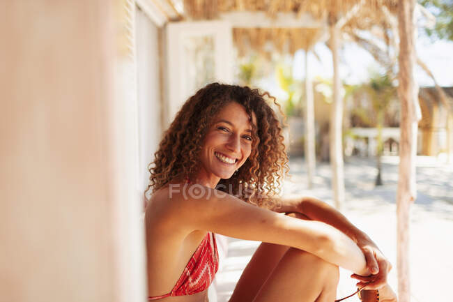 Ritratto felice giovane donna in bikini rilassante sul patio soleggiato della capanna sulla spiaggia — Foto stock