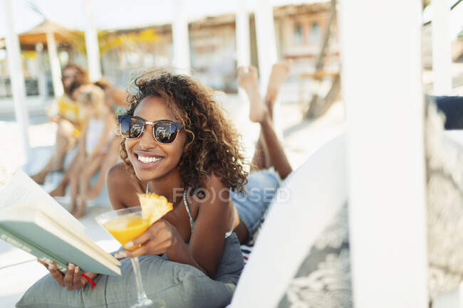 Porträt einer glücklichen, unbeschwerten jungen Frau, die Buch liest und am Strand einen Cocktail trinkt — Stockfoto