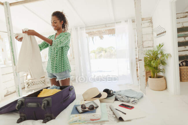 Young woman unpacking suitcase on beach hut bed — Stock Photo