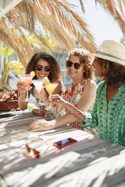 Мать и взрослые дочери пьют коктейли в солнечном пляжном баре — стоковое фото