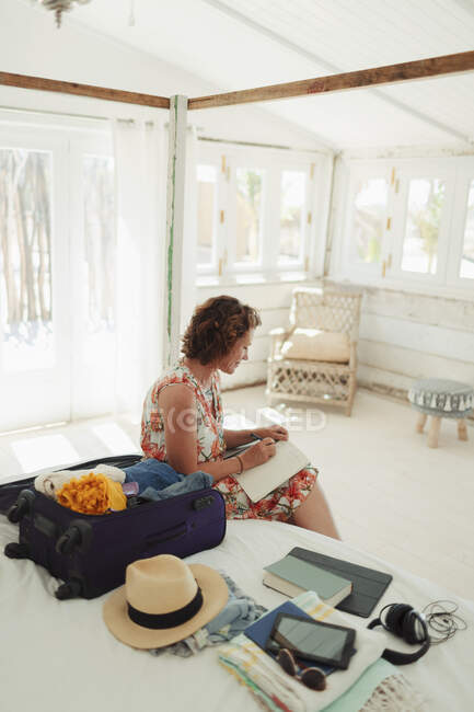 Frau schreibt in Tagebuch neben Koffer im Schlafzimmer einer Strandhütte — Stockfoto
