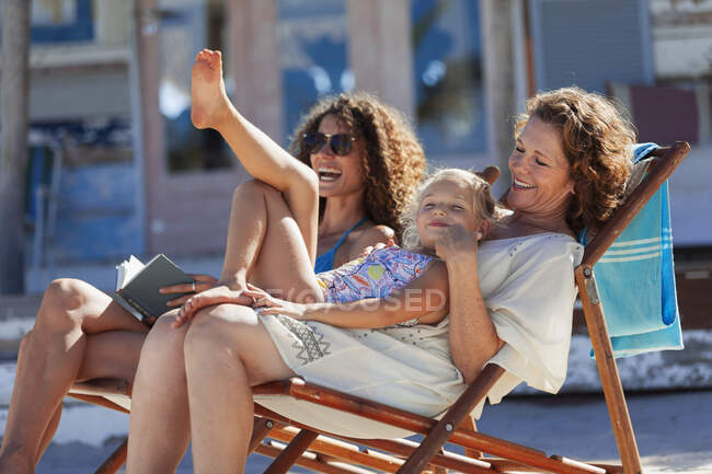 Mujeres juguetonas y felices de varias generaciones relajándose en la playa soleada - foto de stock