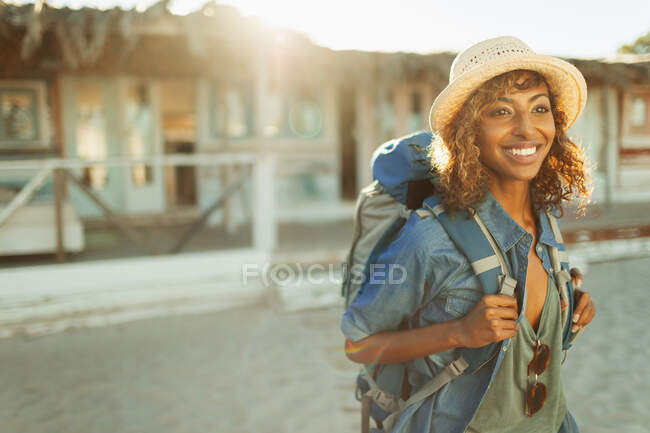 Ritratto felice giovane donna zaino in spalla fuori soleggiata spiaggia capanna — Foto stock