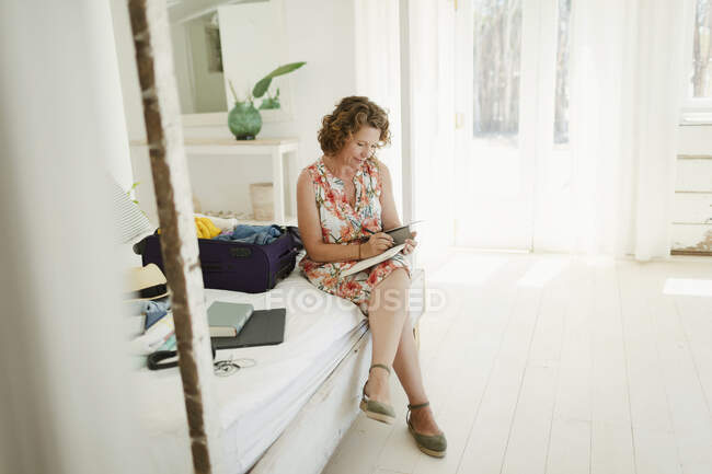 Woman writing in journal next to suitcase on beach hut bedroom — Stock Photo