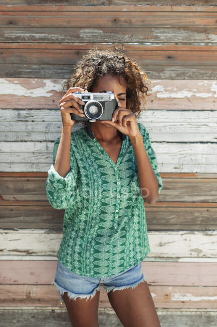 Портрет молодой женщины с помощью ретро-камеры на деревянной доске стены — стоковое фото