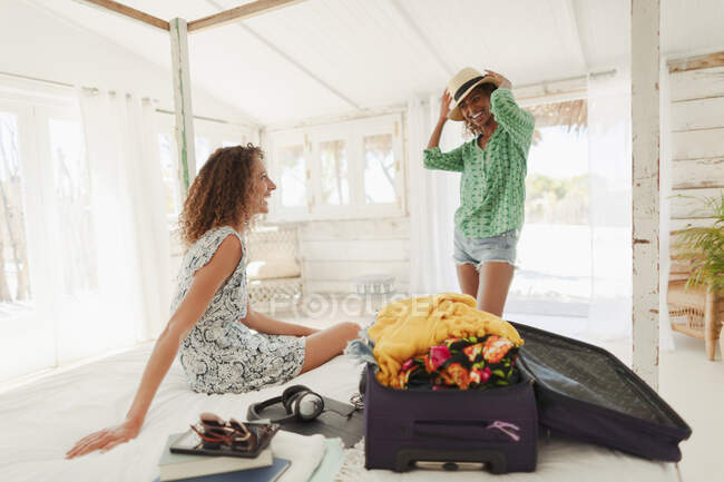 Молодые женщины-друзья распаковывают чемодан в спальне пляжного домика — стоковое фото