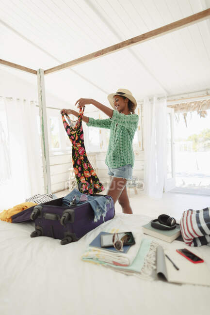 Happy woman unpacking suitcase in beach house bedroom — Stock Photo