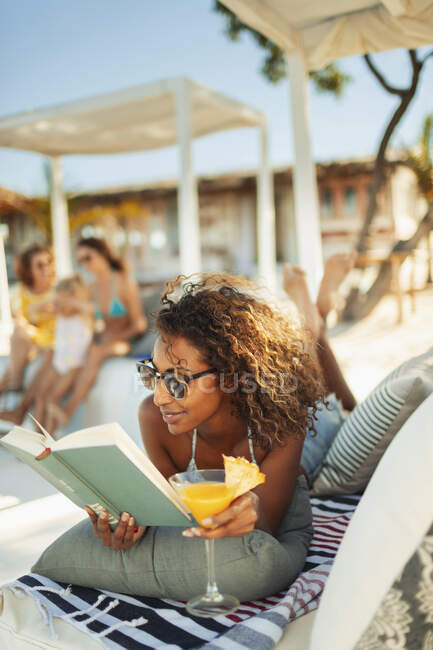 Unbekümmerte Frau entspannt sich, liest Buch und trinkt Cocktail auf Strandterrasse — Stockfoto