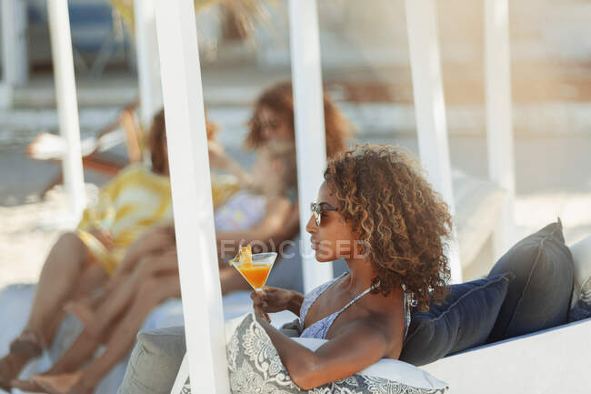 Молодая женщина расслабляется с коктейлем на пляже патио — стоковое фото