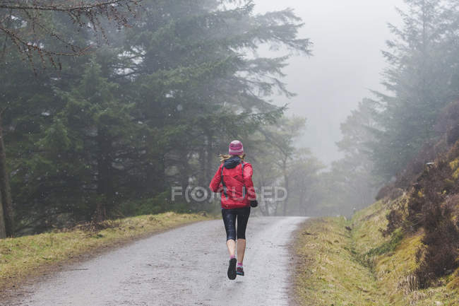 Вид сзади женщины, бегущей под дождем — стоковое фото