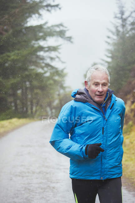 Senior man jogging in rain — Stock Photo