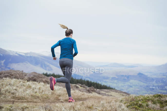 Вид сзади женщины, бегущей по горной тропе — стоковое фото