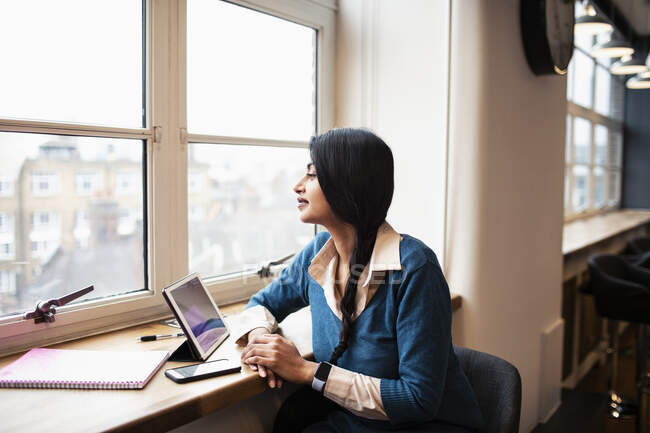 Nachdenkliche Geschäftsfrau arbeitet an digitalem Tablet im Bürofenster — Stockfoto
