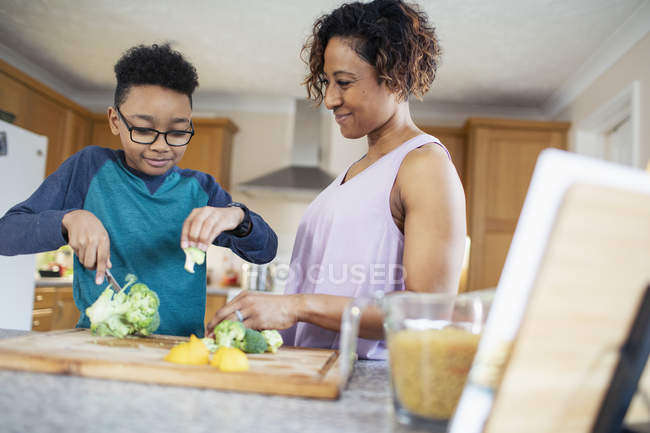 Mother and son cooking, cutting vegetables in kitchen — Stock Photo