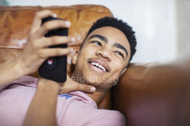 Усміхнений хлопчик-підліток використовує смартфон на дивані — стокове фото