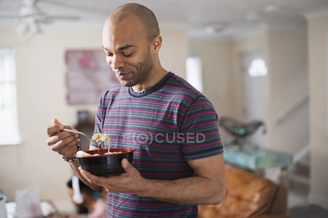 Hombre de pie y comiendo en casa - foto de stock