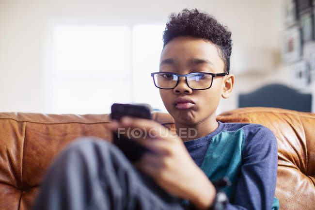 Menino adolescente usando smartphone no sofá — Fotografia de Stock