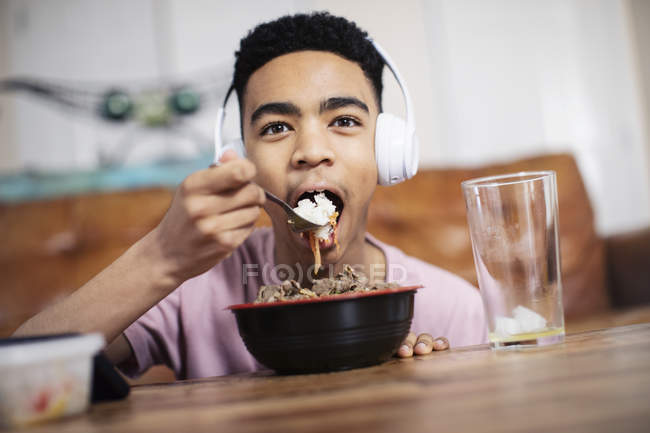 Portrait of teenage boy with headphones eating at coffee table — Stock Photo