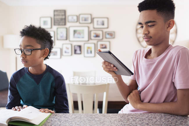 Hermanos leyendo y usando tableta digital en la cocina - foto de stock