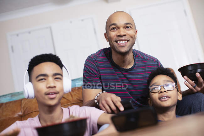 Улыбающиеся отец и сыновья едят и смотрят телевизор — стоковое фото