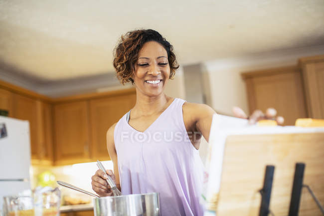 Усміхнена жінка з кулінарною книгою готує на кухні — стокове фото