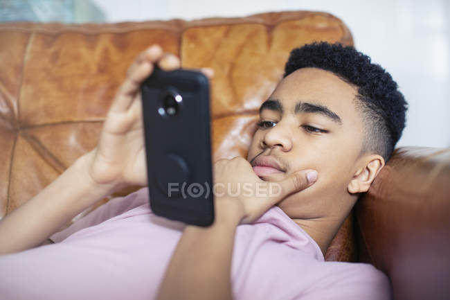 Menino adolescente usando smartphone no sofá — Fotografia de Stock