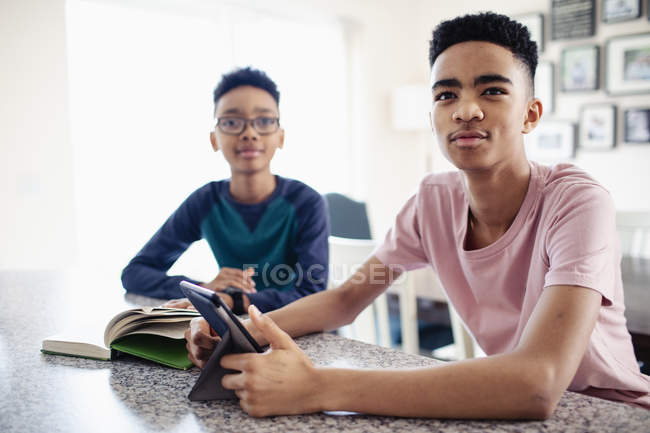 Brothers using digital tablet and reading book in kitchen — Stock Photo
