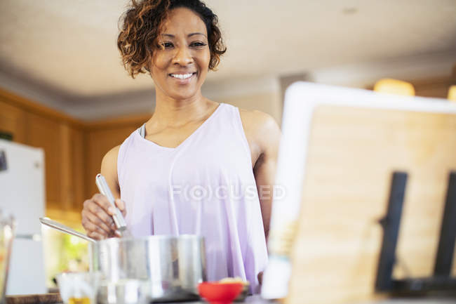 Smiling woman with cookbook cooking in kitchen — Stock Photo